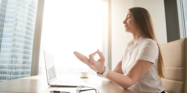 Calm peaceful businesswoman practicing yoga at office desk sitting near laptop, hand in chin mudra yogic gesture, meditation at work, online yoga exercises, practicing breathing, no stress, side view